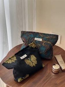 Detail of jacquard makeup bags with butterfly and paisley patterns on a wooden table