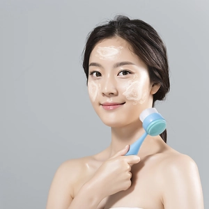 Manual facial brush with soft bristles and silicone massager used on foamy face