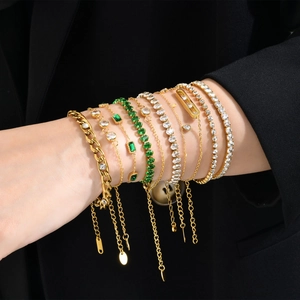 Stackable gold bracelets set with green zircon stones on black suit sleeve background