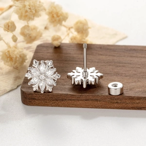 Elegant silver snowflake stud earrings with sparkling cubic zirconia on a rustic wood base
