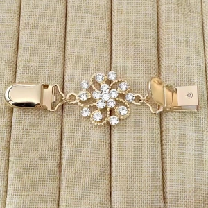 Détail macro de l'attache-pull fleur dorée avec cristaux brillants sur tissu beige