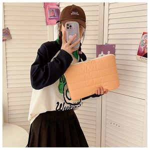 Detailed view of the orange quilted laptop sleeve with stylish zipper closure held by a model