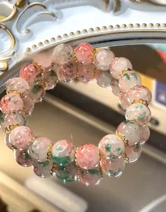 Detail of pink and green cracked glass beads on a reflective mirror with gold spacers