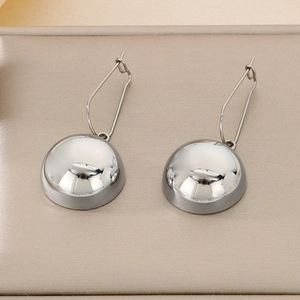 Close-up of polished silver stainless steel hemispherical drop earrings on beige leather
