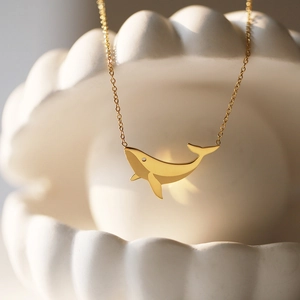 Macro view of a minimalist 18K gold-plated whale pendant resting on a shell bowl