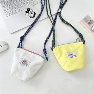 Close-up of stylish mini canvas crossbody bags with colorful labels and braided rope straps