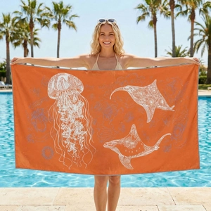 Outdoor model showcasing orange microfiber beach towel with white jellyfish and ray prints