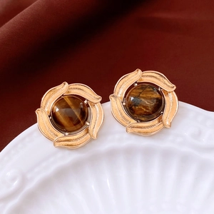 Detail of vintage gold-plated round earrings with tiger eye stone on white plate