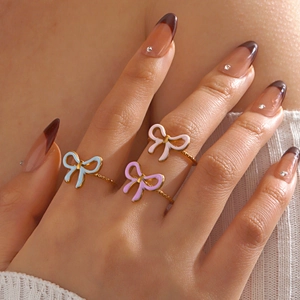 Three colorful enamel bow rings in light blue, purple, and pink on a golden metal base