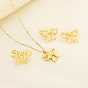 Elegant gold bow jewelry set with necklace earrings and ring on a textured background