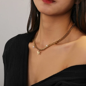 Détail du pendentif papillon doré avec perles sur une grosse chaîne en acier titane