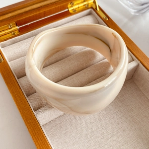 Macro shot of wide marble-patterned resin bangle resting on a natural linen jewelry box