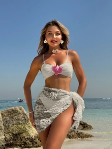 Detailed view of white bikini set with floral accents and lace sarong on beach