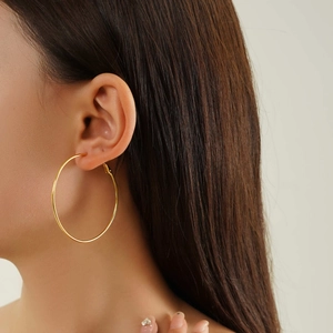 Close-up of model wearing large minimalist golden stainless steel hoop earrings in a side view