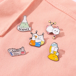 Close-up of five science-themed enamel pins including beakers and molecular structures