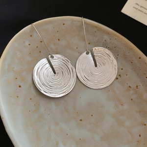 Detail of silver round metal earrings with concentric spiral texture on ceramic plate