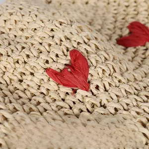 Detailed macro view of handcrafted cream straw hat featuring red crochet heart patterns