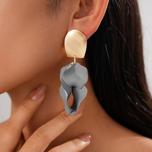 Detail view of gold geometric stud and grey matte pleated petal earrings on a model
