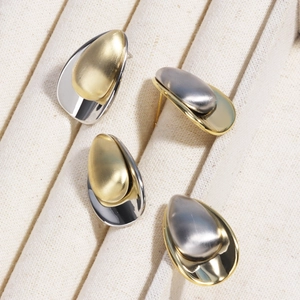 Macro detail of two-tone gold and silver teardrop earrings on a beige textile base