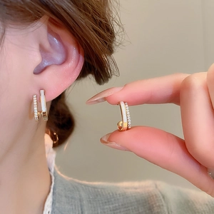 Detailed view of layered C-shaped gold earrings with zircons on a female model