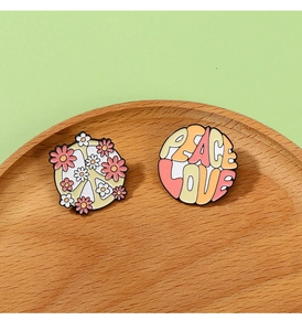 Detailed view of peace and love enamel pins with floral patterns on a wooden tray