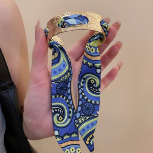 Detail view of golden hammered texture open cuff bracelet with a blue paisley silk scarf