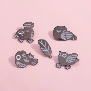 Cinq broches en émail style punk avec oiseaux et plume sur fond rose pastel