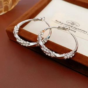 Macro shot of silver twisted hoop earrings with sparkling rhinestones on brown velvet
