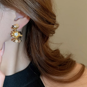 Detailed close-up of triple-layered gold flower earrings with sparkling crystal centers