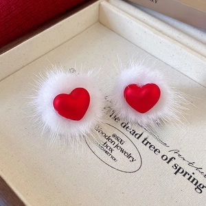 Detail view of red heart-shaped earrings with white faux fur trim in a jewelry box