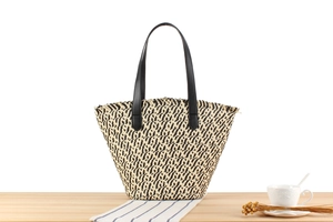 Woven straw tote bag with beige and black stripes and black leather handles on a wooden table