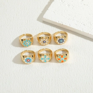 Detail of six gold flower rings with colorful evil eye enamel patterns on a textured surface