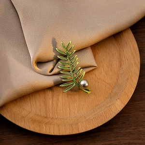 Detail of green leaf brooch with a pearl on beige silk fabric and wood tray
