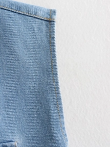 Détail du tissu denim bleu montrant les coutures jaunes et la texture sergée de la veste