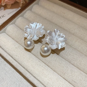 Macro detail of resin flower earrings with elegant pearl pendant on velvet tray