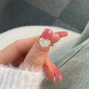 Close-up of heart-cut sparkling gemstone ring with golden band on model's finger