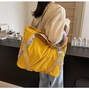 Détail du grand sac cabas en nylon jaune avec une bandoulière rayée et lettrages chic