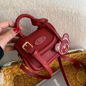 Red mini PU leather handbag with bear charm shown held by hand in a lifestyle setting