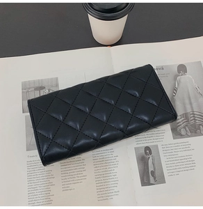 Close-up of quilted black long wallet on a fashion magazine next to a coffee cup