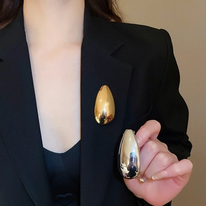 Close-up of minimalist gold and silver teardrop brooches on a black blazer lapel