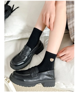 Close-up of golden bear embroidery on black crew socks paired with black platform loafers