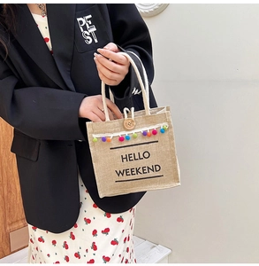 Detail of linen tote bag with multi-colored pom-poms and HELLO WEEKEND text