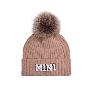 Close-up of pink knit hat featuring a brown faux fur pompom and MINI letter embroidery