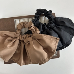Detail of black and brown satin scrunchies with pleated double-layer ruffles on a wooden tray