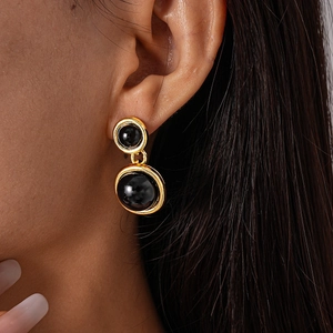Macro shot of vintage gold earrings with black resin spheres worn by a model