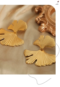 Detail of golden ginkgo leaf earrings with layered textures on champagne silk background