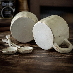 Handmade ceramic mug set with speckled glaze and matching spoons on a wooden table