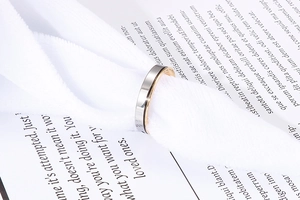 Bague élégante bicolore en acier titane présentée sur un ruban et une page de livre