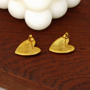 Detail of gold heart stud earring with radiating texture on a dark wood background