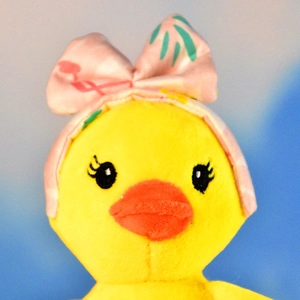 Close-up of cute yellow duck plush keychain wearing a pink tropical bow headband